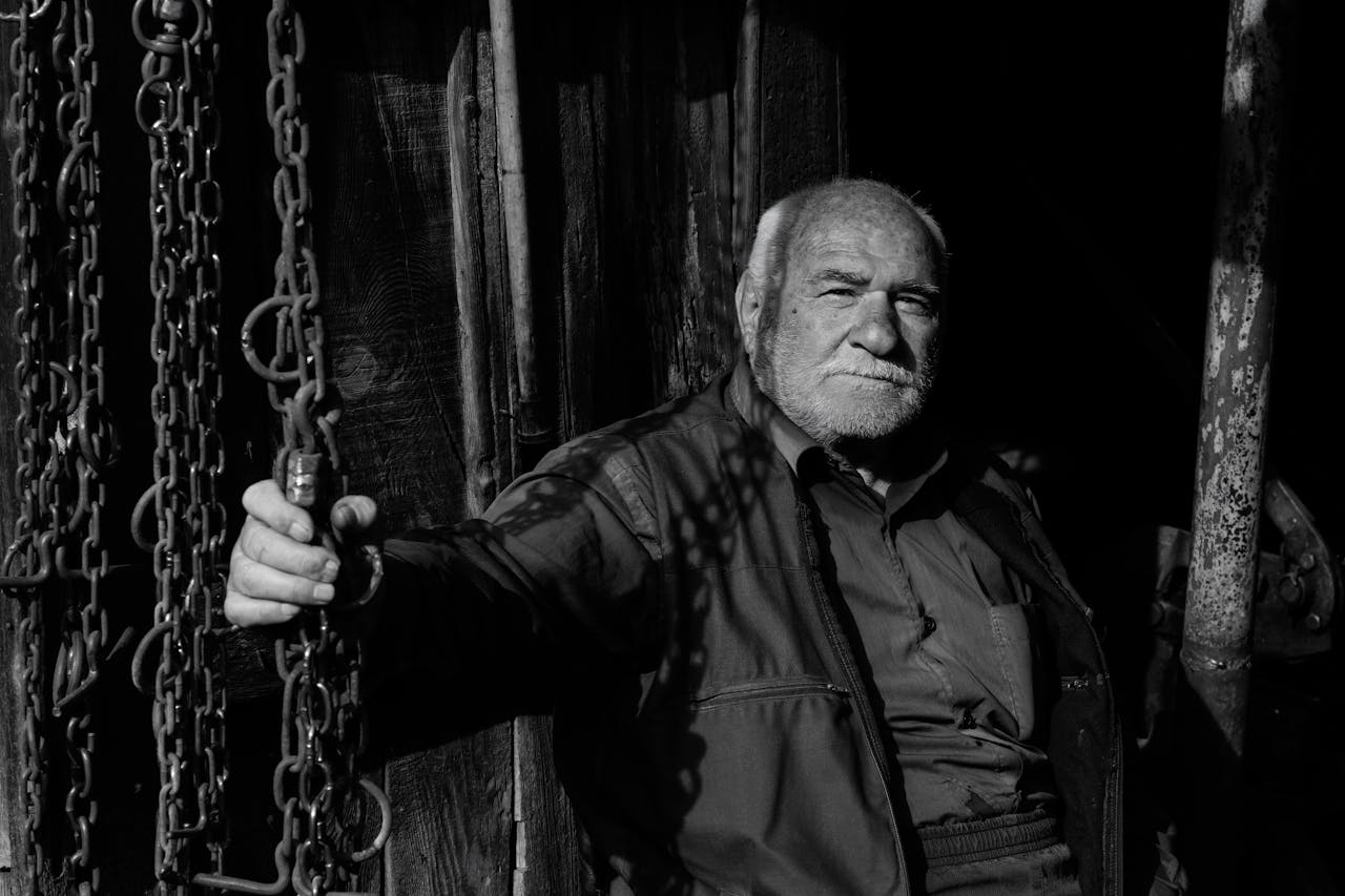 Black and white portrait of an elderly man grasping a chain, evoking a sense of solitude and strength.