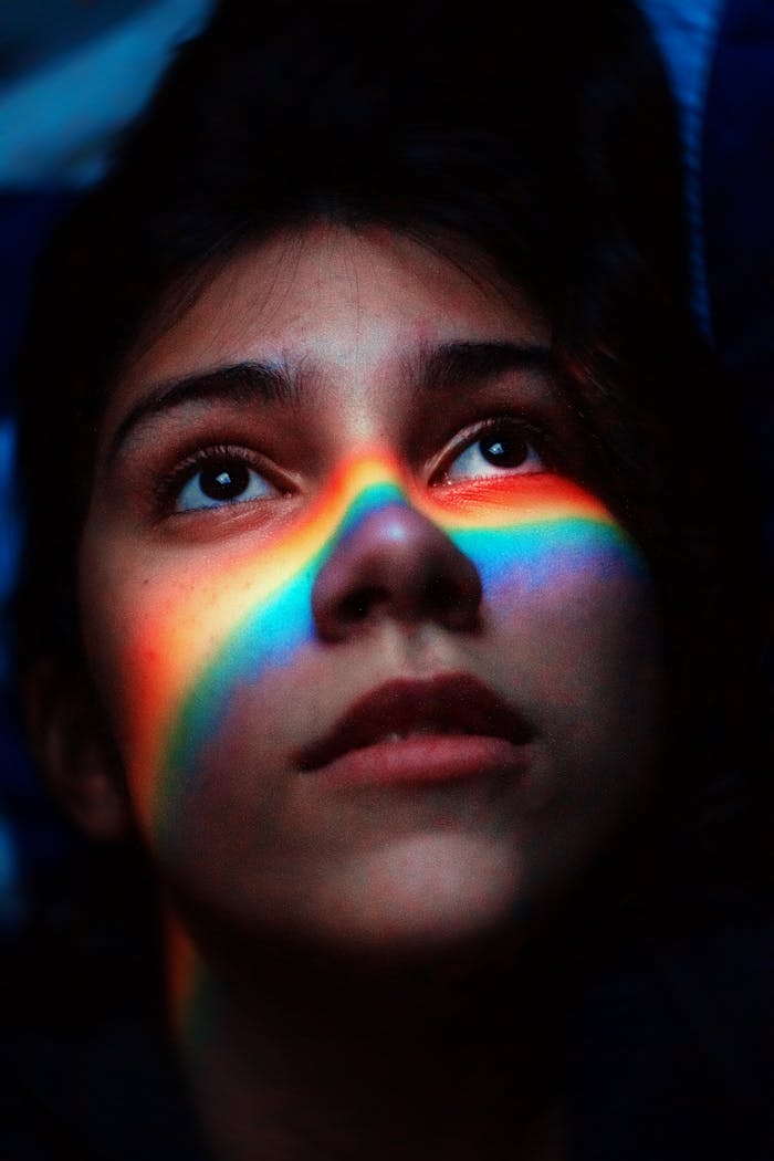 Portrait of a woman with a rainbow light across her face, capturing a moody and artistic feel.